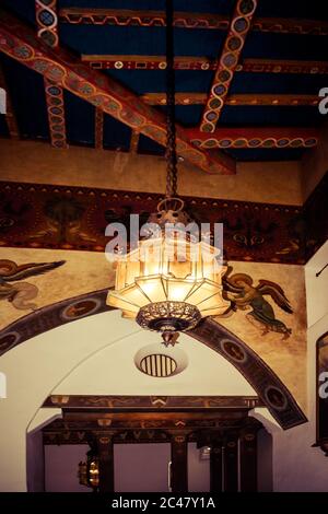 Lanterna pendente in metallo spagnolo appesa a colorati soffitti con travi in legno con murales e accenti decorativi all'interno del tribunale della contea di Santa Barbara Foto Stock