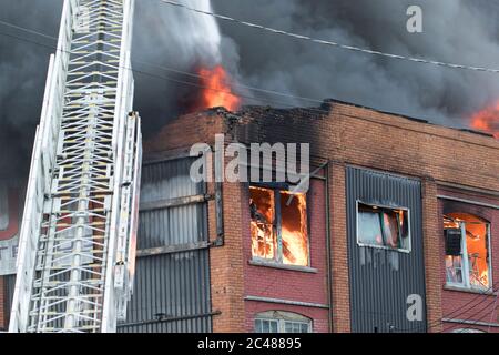 Incendio che brucia all'interno di un grande edificio da vicino. Fumo pesante e fiamme che si propagano dall'interno di un incendio a più strutture di allarme. Foto Stock