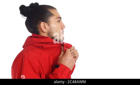 Giovane ispanico con i capelli raccolti arco fatto indossare t-shirt nera e giacca rossa, mani che stretching la giacca, profilo in posa guardando a destra Foto Stock