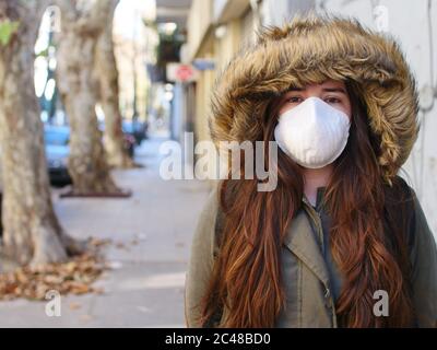 Una giovane ragazza sullo sfondo di una strada vuota indossa una maschera facciale che protegge contro la diffusione del coronavirus COVID malattia primo piano di una donna Foto Stock