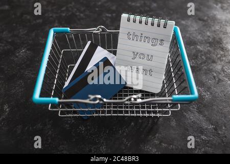 concetto di budget e shopping, tthings si desidera blocco note nel carrello della spesa con carte di credito Foto Stock