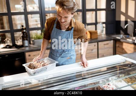 Ritratto di un bel venditore che lavora con gelato al banco della pasticceria o del caffè Foto Stock