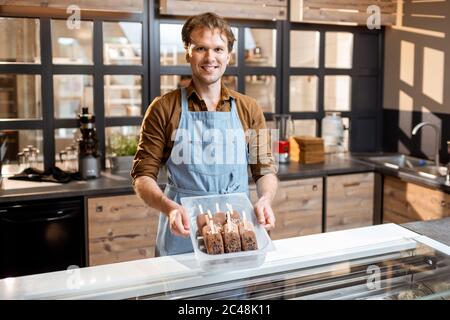 Ritratto di un bel venditore che lavora con gelato al banco della pasticceria o del caffè Foto Stock