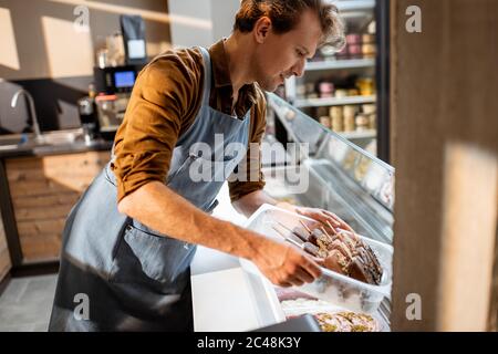 Ritratto di un bel venditore che lavora con gelato al banco della pasticceria o del caffè Foto Stock