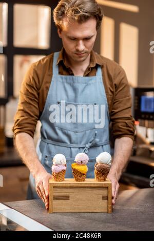 Venditore che mette un supporto con tre gelati yummy in coni di cialda con sapore diverso sul banco di un negozio Foto Stock