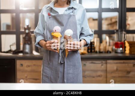 Venditore femminile che tiene due gelati yummy nel cono del waffle al negozio, primo piano Foto Stock