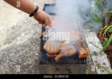 Uomo grigliare le succulente bistecche di carne di maiale marinate crude in griglie grigliate nel cortile di casa in estate Foto Stock