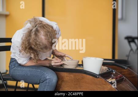 Tagli di prodotto con filo. Mani artigiane che fanno ciotola di ceramica. Donna che lavora sulla ruota del vasaio. Il business shop per famiglie sculta il vaso da argilla. Foto Stock