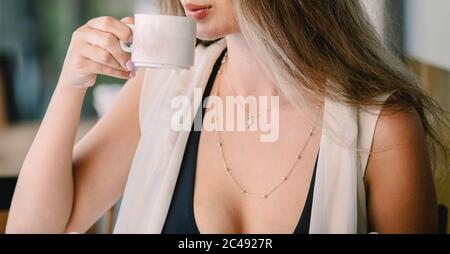 Caffè. Bella ragazza che beve tè o caffè al caffè. Donna modello di bellezza con la tazza di bevanda calda. Colori caldi tonati. Foto Stock