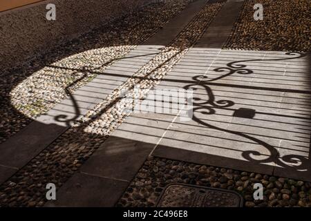 L'ombra contrastante di un elaborato cancello in ferro battuto su un marciapiede di ciottoli nel centro storico di Brescia (Lombardia, Italia). Foto Stock