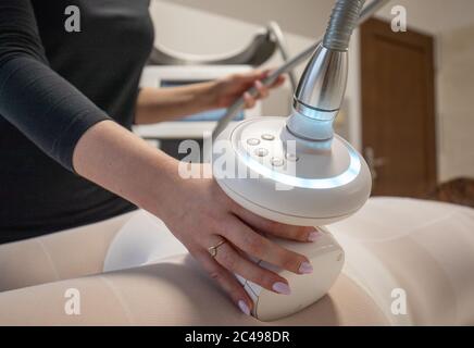 Donna in tuta bianca che ottiene massaggio anticellulite con apparecchio GPL. Trattamento effettuato da terapista professionista in clinica cosmetologica Foto Stock