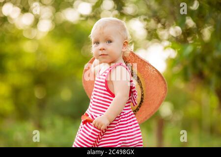 Carino bambina in un vestito rosso e cappello cammina in estate a piedi nudi sull'erba verde, spazio per il testo Foto Stock