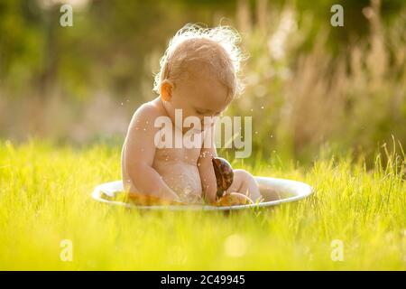 Carina bambina si siede in un bacino d'acqua estiva sull'erba verde Foto Stock