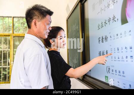 (200625) -- NINGMING, 25 giugno 2020 (Xinhua) -- Jiao Lingxia mostra suo padre Jiao Shengding come usare il touch screen per insegnare in un luogo di insegnamento in Aidian Township della Contea di Ningming, regione autonoma di Guangxi Zhuang, 23 giugno 2020. Jiao Shengding, 52 anni, è l'unico insegnante del villaggio di Zhangji, situato al confine tra Cina e Vietnam. Dopo essersi laureato alla scuola professionale secondaria della contea nel 1990, Jiao ha scelto di essere un insegnante presso il suo villaggio di Zhangji, città natale, e da allora ha insegnato lì per 30 anni. Nel passato Foto Stock