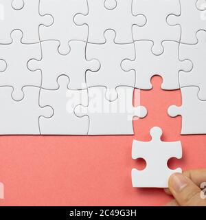 Set di pezzi di puzzle bianchi e mano che tiene ultimo pezzo Foto Stock