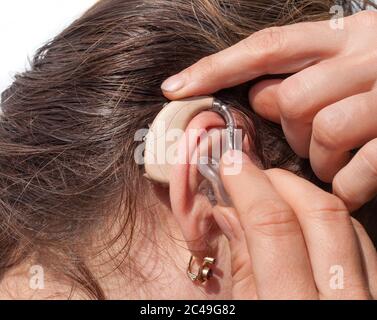 Primo piano di una donna che inserisce un apparecchio acustico nell'orecchio Foto Stock