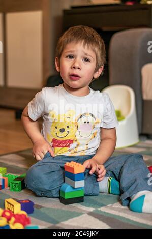 POZNAN, POLONIA - 30 maggio 2020: Piccolo infelice bambino di due anni che gioca con blocchi Lego Duplo su un pavimento in una casa. Foto Stock