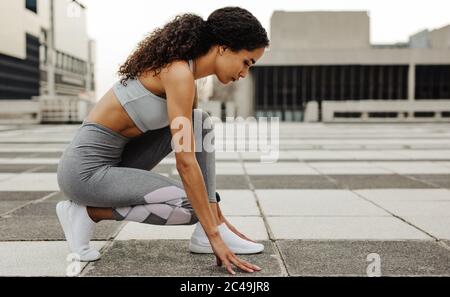 Vista laterale di una sprinter femminile in posizione iniziale all'aperto in città. Atleta donna in posizione iniziale. Foto Stock