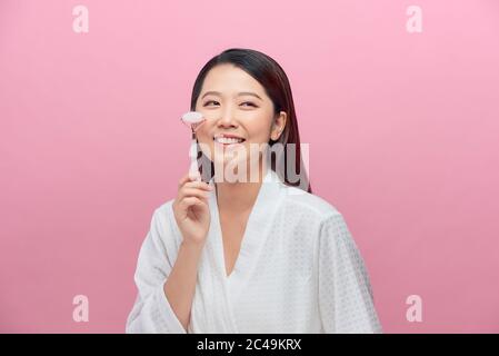 Bella donna asiatica usa il rullo di giada per massaggiare il suo viso Foto Stock