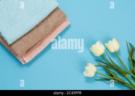 Pile di morbidi asciugamani di spugna con tulipani su sfondo blu. Vista dall'alto. Foto Stock