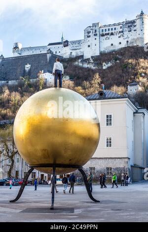 Salisburgo, Austria - 5 marzo 2017: Scultura di un uomo in piedi su una palla d'oro a Kapitelplatz, nel centro storico di Salisburgo e nella fortezza di Hohensalzburg Foto Stock