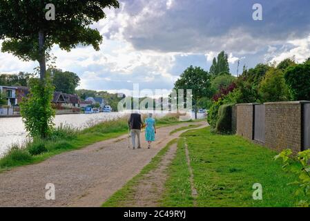 Vista posteriore di una vecchia coppia che tiene le mani mentre passeggi sul sentiero sul Tamigi a Laleham in una serata estiva Surrey England UK Foto Stock