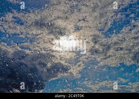 Primo piano di gocce di pioggia su una finestra sullo sfondo del sole, nuvole di pioggia e cielo blu Foto Stock