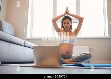 Signora curiosa che fa yoga con lezioni online a casa Foto Stock
