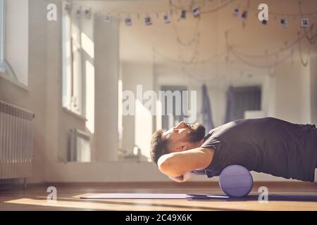 Uomo bearded giacente sul rullo di schiuma durante l'addestramento in studio Foto Stock