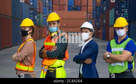 I lavoratori industriali o i tecnici che indossano maschere di protezione Coronavirus o COVID-19 si trovano di fronte al contenitore di spedizione. Foto Stock