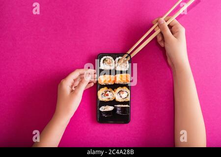 Fruste da donna e telefono cellulare con gustoso sushi rotola sullo schermo su sfondo a colori. Concetto di consegna di cibo online. Spazio di copia Foto Stock