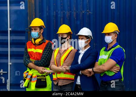 I lavoratori industriali o i tecnici che indossano le maschere di protezione Coronavirus o COVID-19 sono attraversati e si trovano di fronte al contenitore di spedizione. Foto Stock