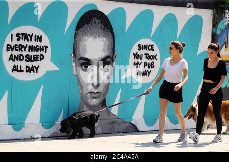 La gente cammina i loro cani davanti al murale dell'artista irlandese emmalene Blake del cantante Sinead o'Connor vicino al sito del vecchio pub Bernard Shaw a Dublino, chiuso alla fine dell'anno scorso. I pub e i bar dell'hotel che operano come ristoranti possono iniziare la riapertura al pubblico lunedì 29 giugno, in linea con la fase 3 del Governo di alleggerire le restrizioni COVID-19. Foto Stock