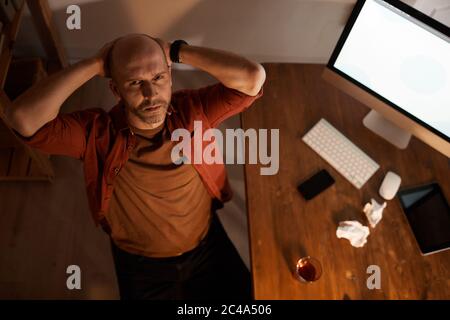 Ritratto di un uomo maturo calvo seduto sul suo posto di lavoro e guardando la fotocamera che egli contempla circa il futuro progetto in serata Foto Stock