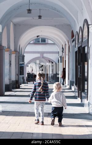 Due bambini camminano insieme a mano nella vecchia strada porticata della città. Amore di famiglia e tema di amicizia. Foto Stock