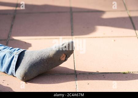 Piede ragazzo con jeans e sn vecchio calzino con un buco in esso esterno Foto Stock