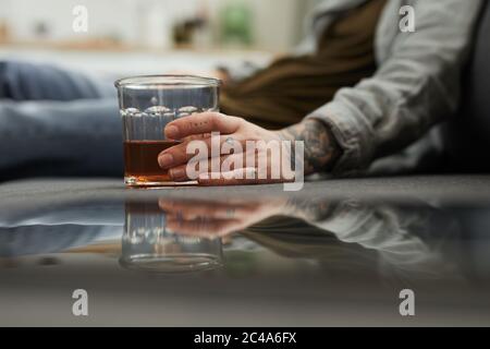 Primo piano di giovane donna con bicchiere di whisky seduto a terra e bevendo a casa Foto Stock