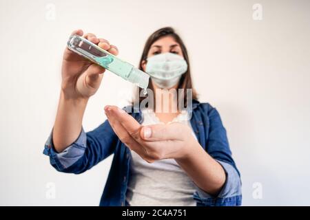 Donna con maschera di protezione medica che mette su antisettico per disinfettare le mani Foto Stock