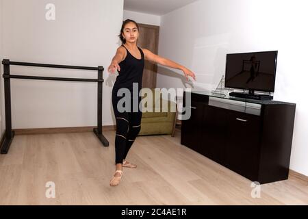 la ragazza adolescente pratica balletto, danza, ginnastica a casa con lezioni di internet Foto Stock