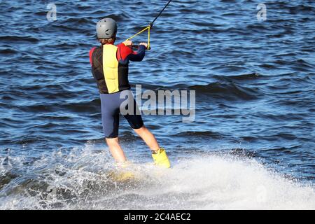 Wakeboarding in giornata di sole, l'uomo esegue un trucco in uno spruzzo d'acqua. Surfista nel parco di wake, sport estivi Foto Stock