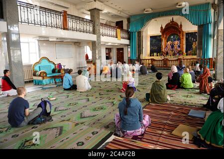 Seguaci di Krishna seduti su un pavimento e ascoltando la predicazione dei guru in un tempio Foto Stock