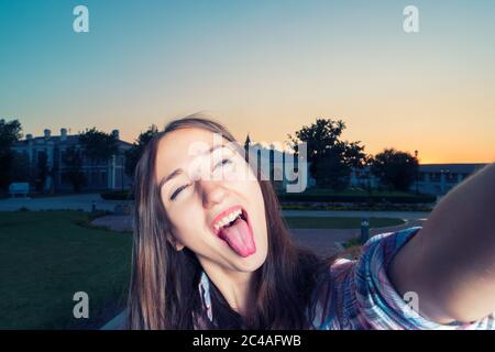 Giovane ragazza divertente sta facendo selfie divertirsi con la sua lingua è sticking out Foto Stock