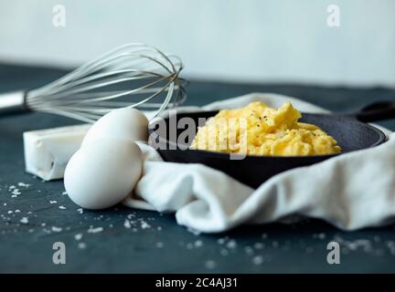 Deliziose uova strapazzate in padella in ghisa con whisk, burro e uova Foto Stock