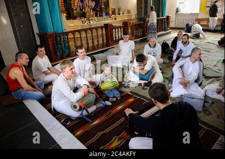 Gruppo di giovani musicisti, seguaci di Krishna, seduti sul pavimento nel tempio con strumenti musicali Foto Stock