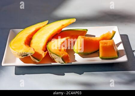 Melone al miele o melone cantalupo Cucumis melo. Affettato di melone giapponese su piatto bianco con ombre. Frutta estiva. Concetto di assistenza sanitaria. Messa a fuoco selettiva Foto Stock