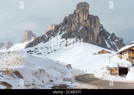 Vuota e tortuosa strada libera di neve in uno scenario invernale di montagna nelle Dolomiti in una giornata nuvolosa Foto Stock