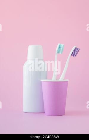 Due spazzolini da denti in una tazza rosa e collutorio in una bottiglia su sfondo rosa, concetto di igiene orale Foto Stock