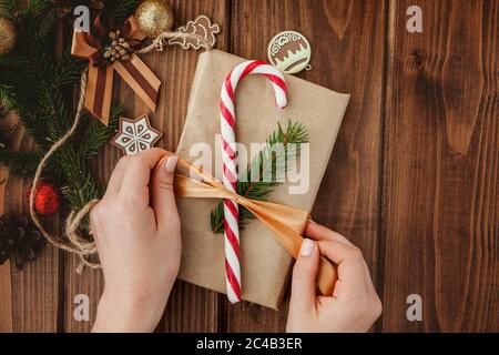 Donna s mani incarto regalo di Natale, vicino. Impreparati i regali di natale su sfondo di legno con elementi di arredamento e oggetti, vista dall'alto. Natale Foto Stock