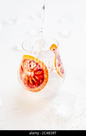 Preparare un cocktail ghiacciato frizzante con arancio di sangue su sfondo bianco Foto Stock