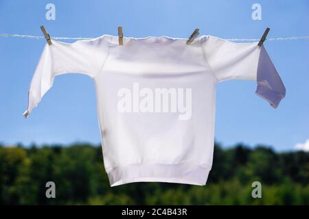 Bianco pullover mockup appeso di fronte al cielo blu e verde alberi sfondo. Il maglione è appeso su una corda con gli abiti. Concept estivo in mock-up. Foto Stock